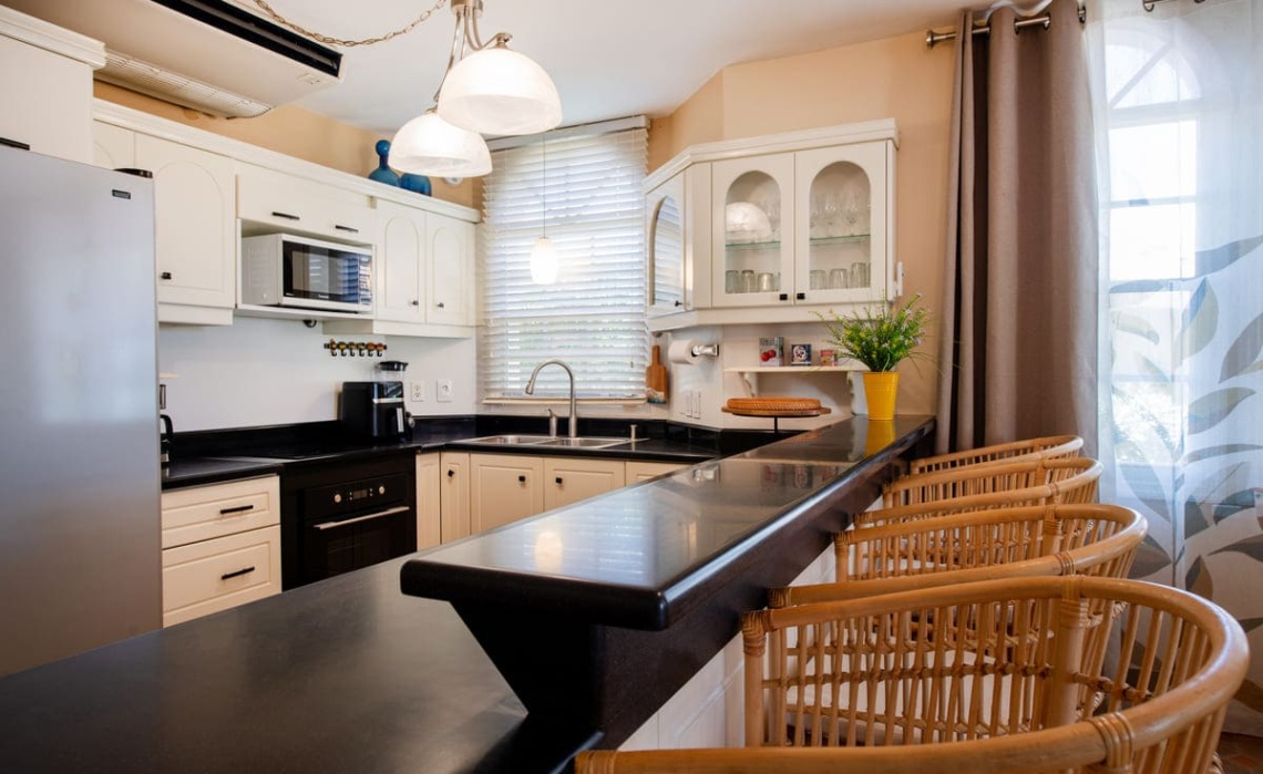 Open‑plan dining space in the Portofino two‑bedroom apartment, showing a table with chairs and a fully equipped kitchen behind, including refrigerator/freezer, dishwasher, oven, cooktop, microwave, air‑fryer, electric kettle and Nespresso coffee machine.