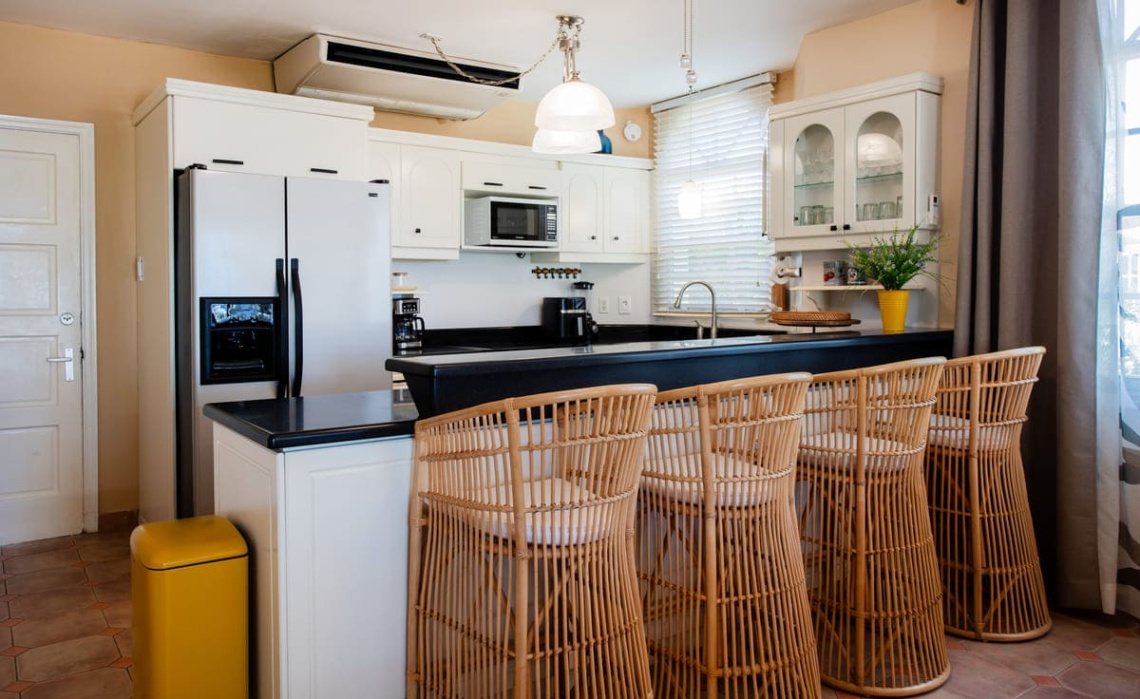 Open‑plan dining area of the Portofino two‑bedroom apartment, showing a table with chairs and a fully equipped kitchen behind, including refrigerator/freezer, dishwasher, oven, cooktop, microwave, air‑fryer, electric kettle and Nespresso coffee machine.