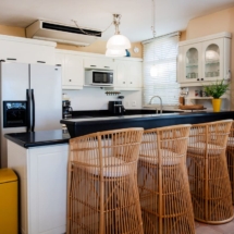 Open‑plan dining area of the Portofino two‑bedroom apartment, showing a table with chairs and a fully equipped kitchen behind, including refrigerator/freezer, dishwasher, oven, cooktop, microwave, air‑fryer, electric kettle and Nespresso coffee machine.