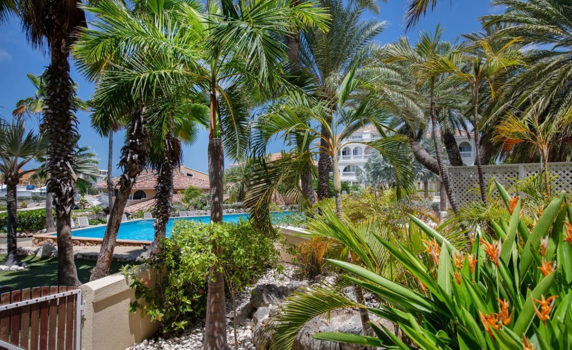 Private tropical garden of the Portofino two‑bedroom apartment leading to a covered terrace that overlooks the swimming pool, surrounded by palm trees