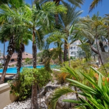 Private tropical garden of the Portofino two‑bedroom apartment leading to a covered terrace that overlooks the swimming pool, surrounded by palm trees