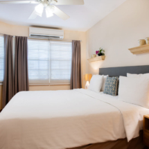 Primary bedroom of the Portofino apartment featuring a king‑size bed, walk‑in closet and en‑suite bathroom, with blinds, curtains, air‑conditioning and ceiling fan.