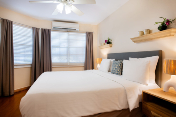 Primary bedroom of the Portofino apartment featuring a king‑size bed, walk‑in closet and en‑suite bathroom, with blinds, curtains, air‑conditioning and ceiling fan.